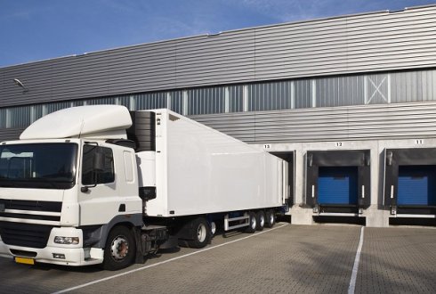 Een afbeelding van een vrachtwagen die met de achterkant staat te lossen tegen een metaal grijs gebouw